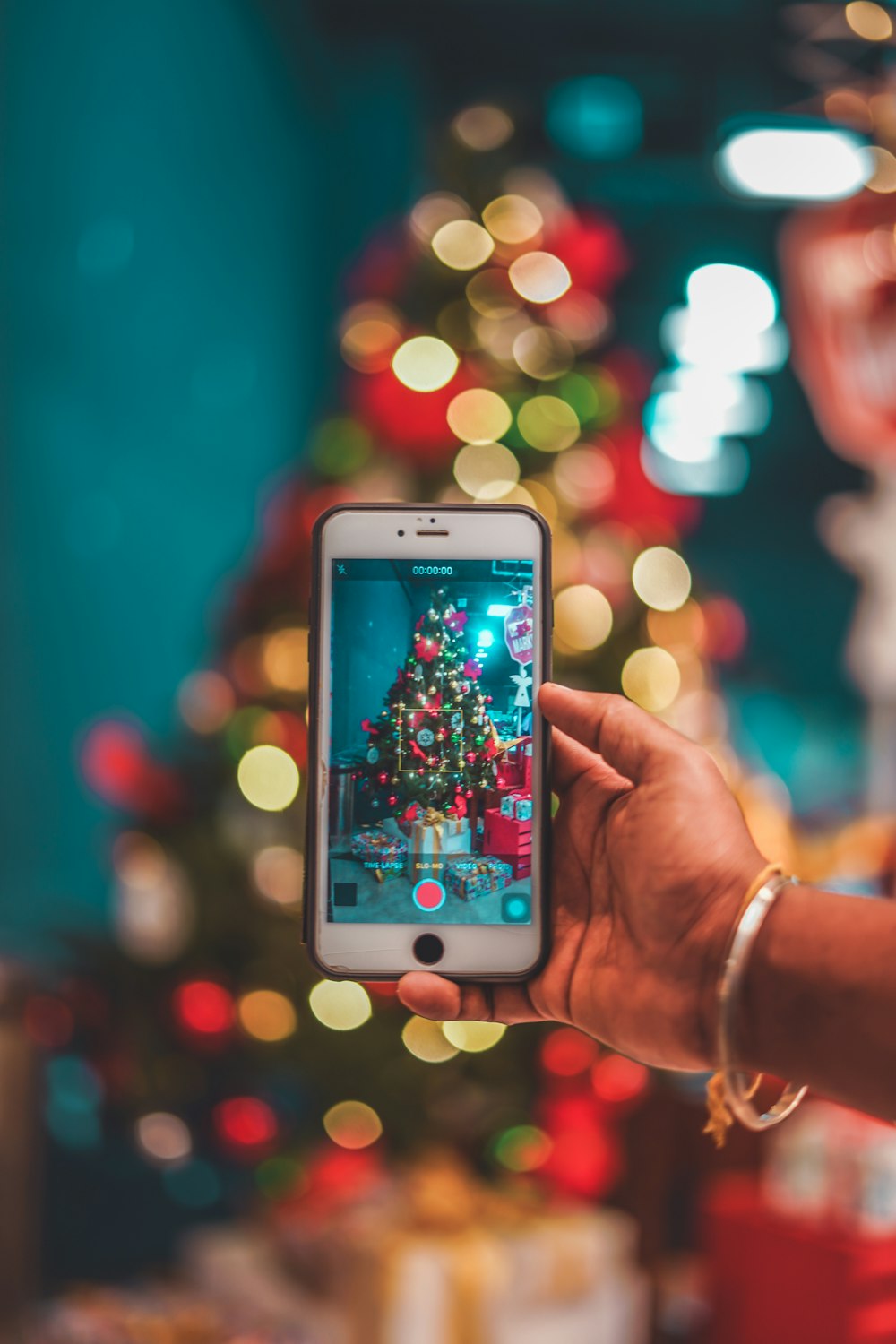 a person holding a cell phone in front of a christmas tree