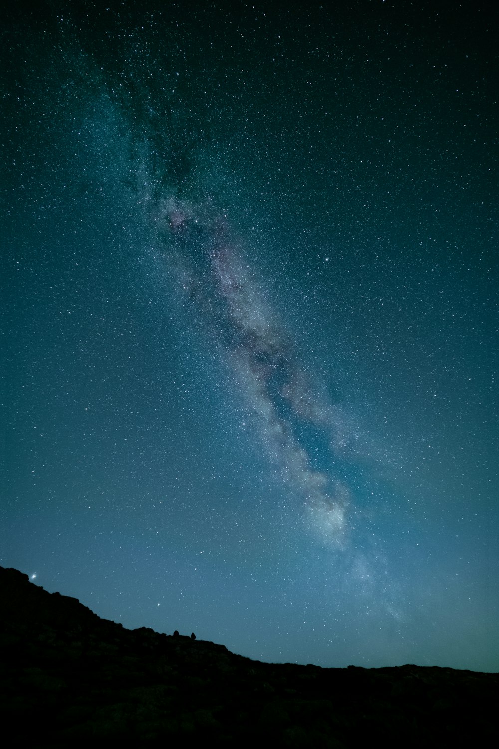 a man standing on top of a hill under a sky filled with stars