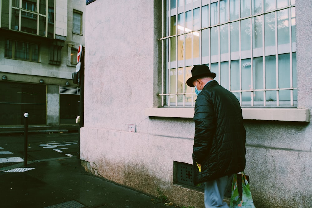 a man in a black jacket and hat standing next to a building