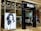 The entrance of a modern hair salon named Rush features sleek glass doors. Inside, the salon is stylishly presented with black chairs and lit mirrors. A large monochrome advertisement poster displays a model with voluminous hair, enhancing the salon's chic interior.