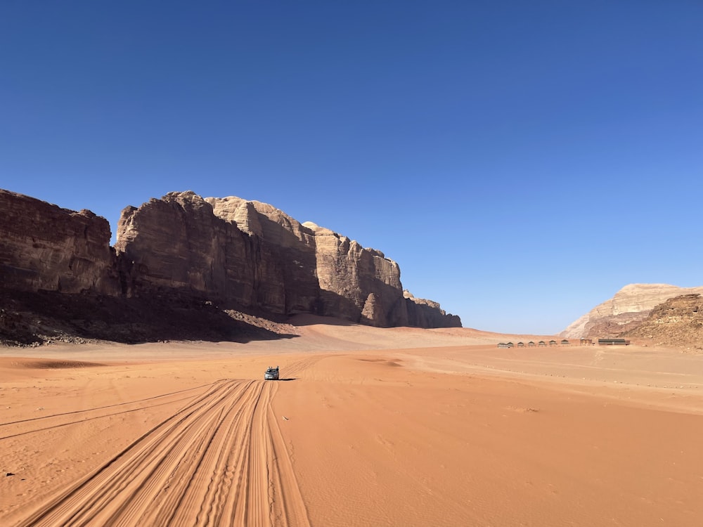 a jeep driving through the desert with a mountain in the background