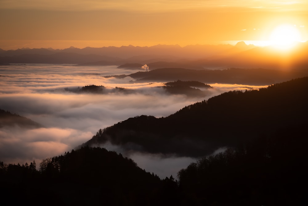 the sun is setting over the mountains covered in fog