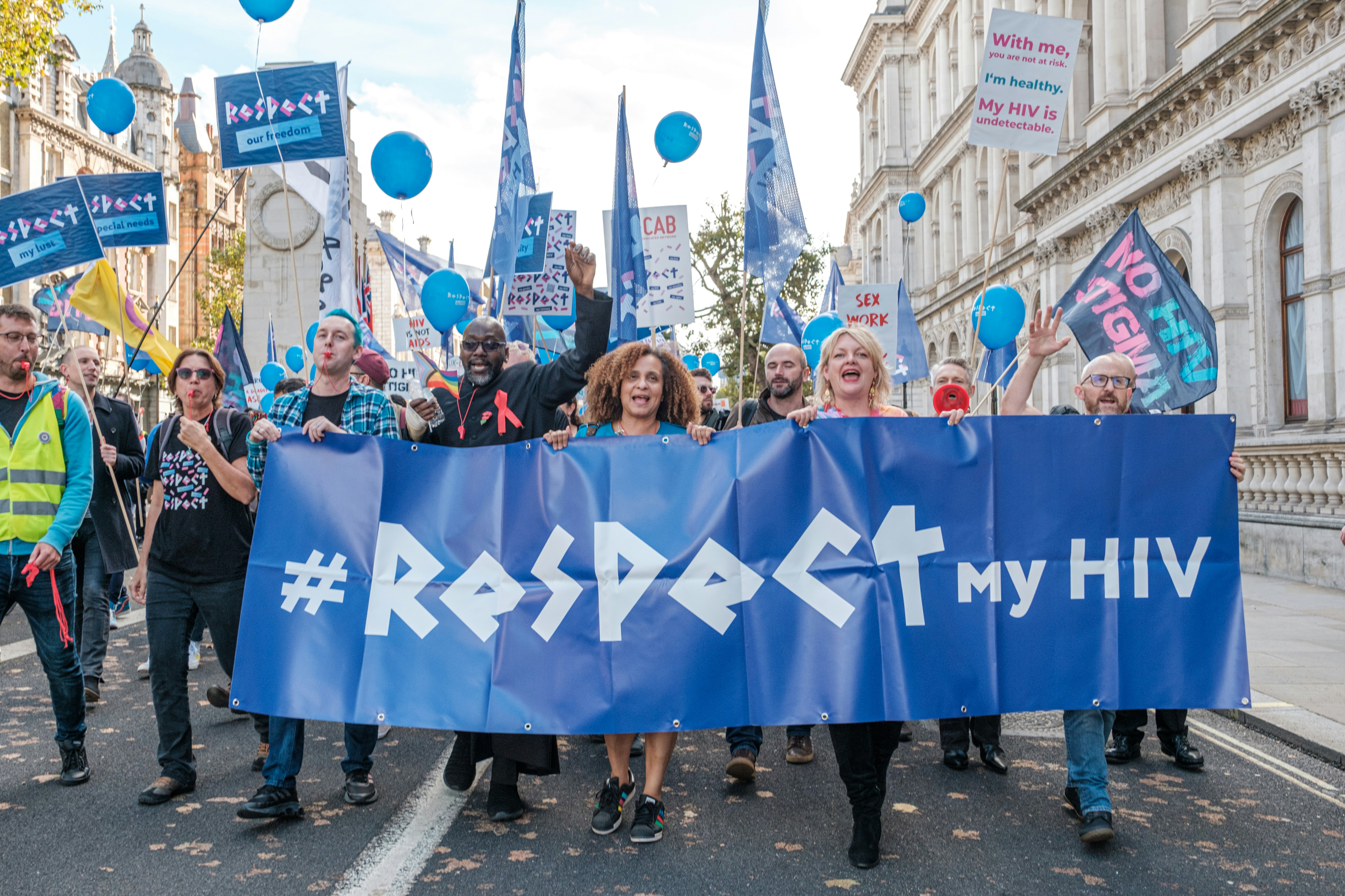Image of a diverse group of protesters holding signs advocating for HIV awareness and rights.