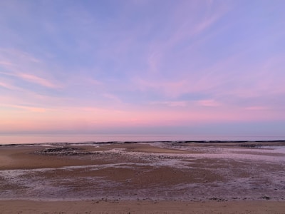 A serene Mediterranean beach at dusk with pastel pink and orange skies.
