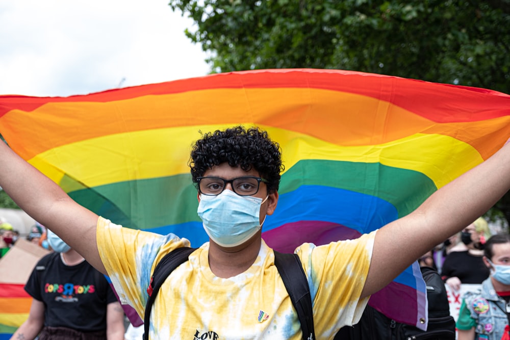 a man wearing a face mask holding a rainbow flag