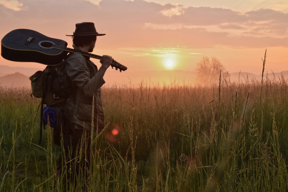 a man standing in a field holding a guitar