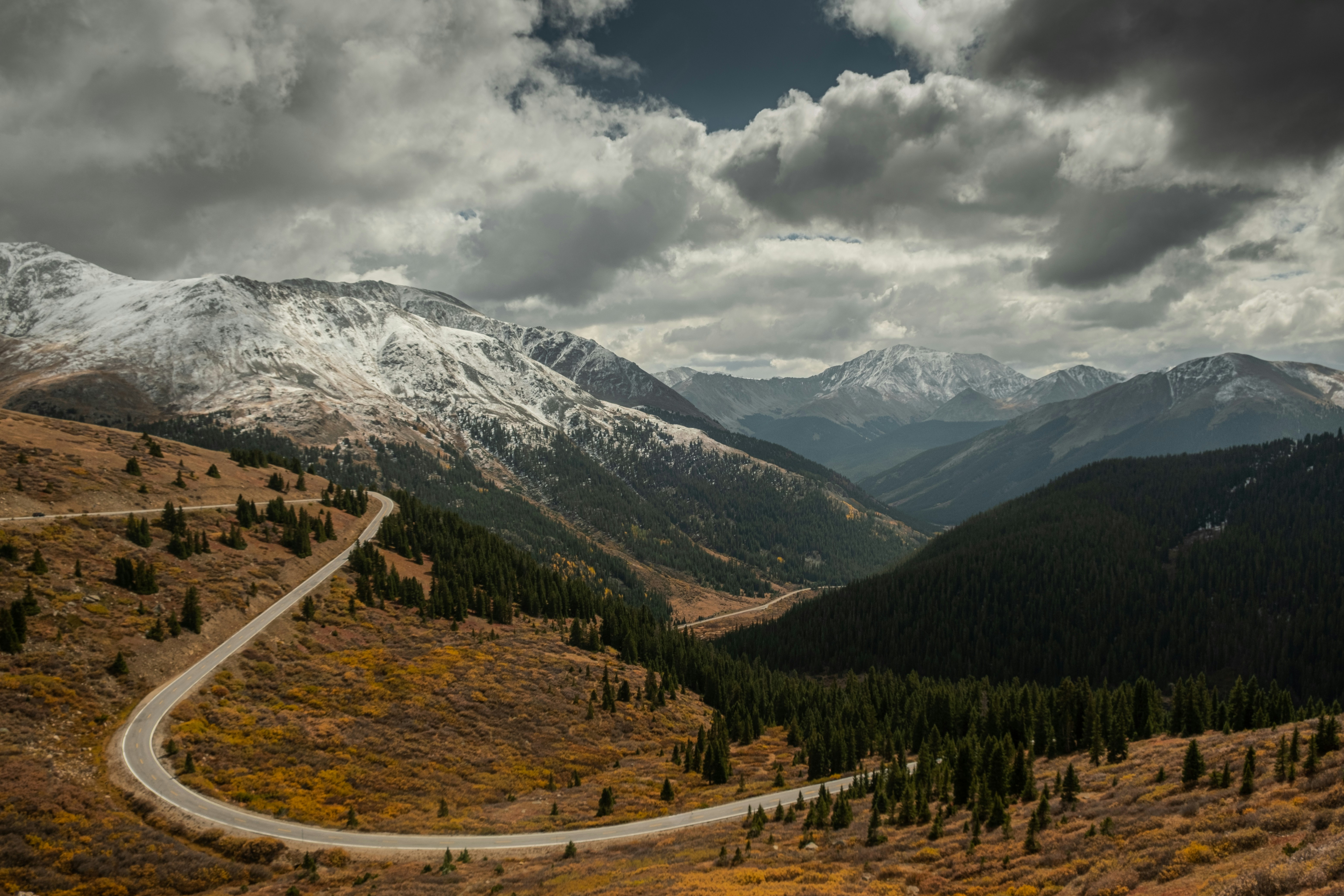 a winding road in the mountains under a cloudy sky
