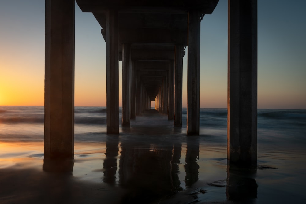 the sun is setting at the end of a pier