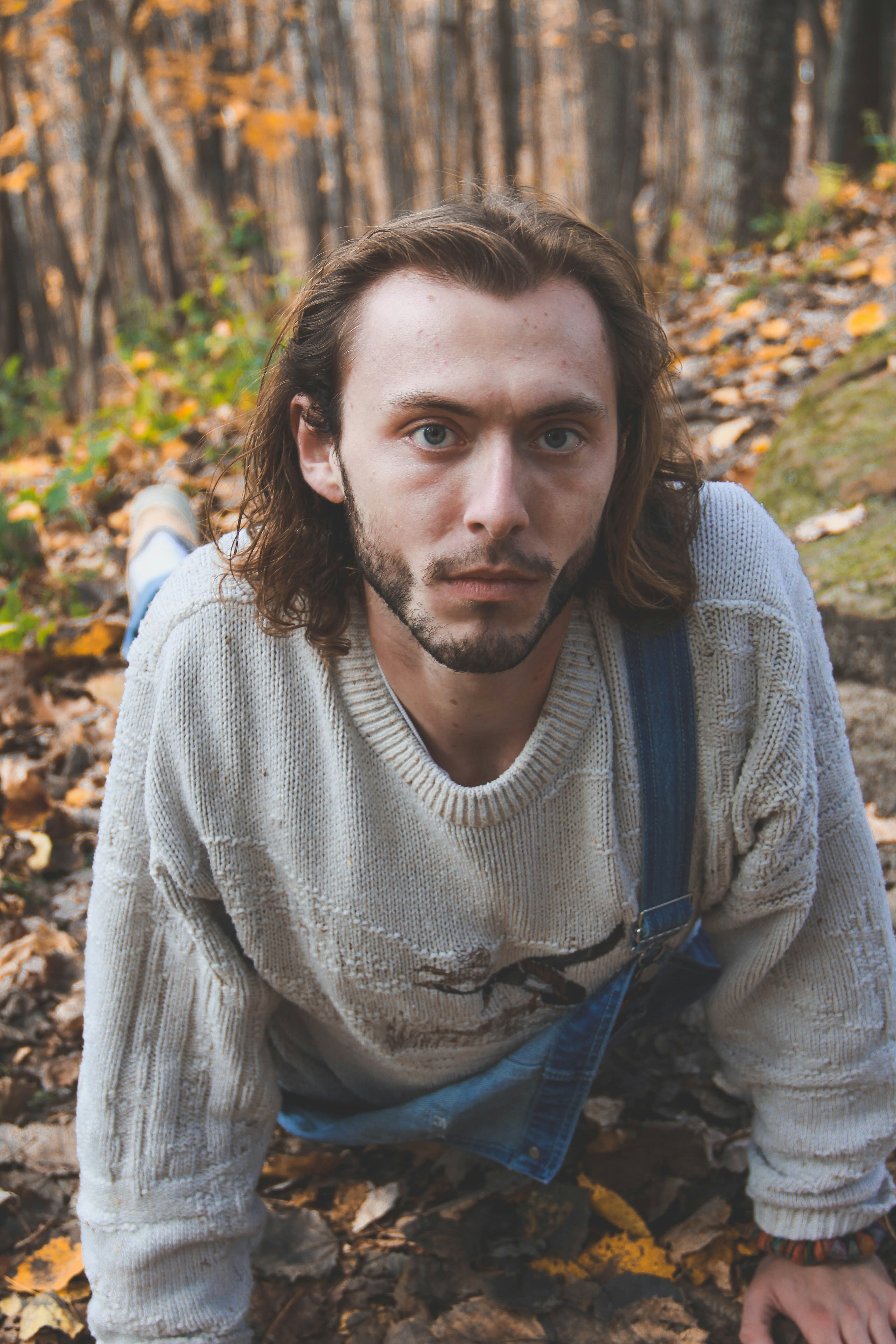 a man with long hair and suspenders sitting in leaves