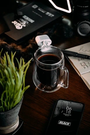 Black and white photo of a cozy workspace with a laptop, notebook, and coffee cup.