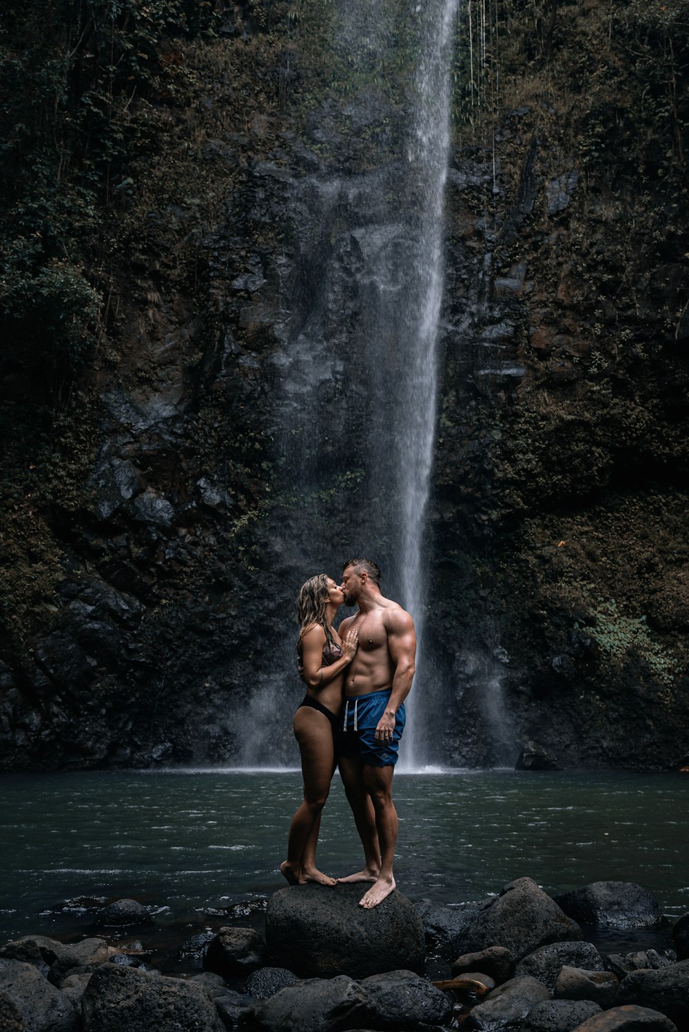 a man and a woman standing in front of a waterfall