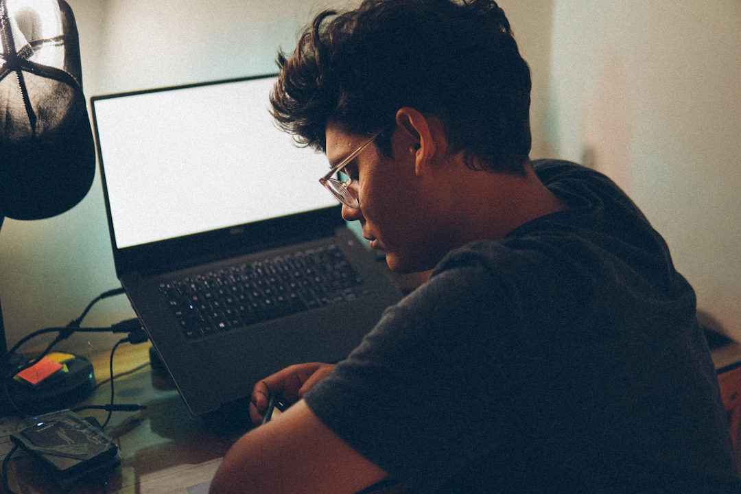 A young engineer teaching himself to code on a laptop at a cluttered home desk