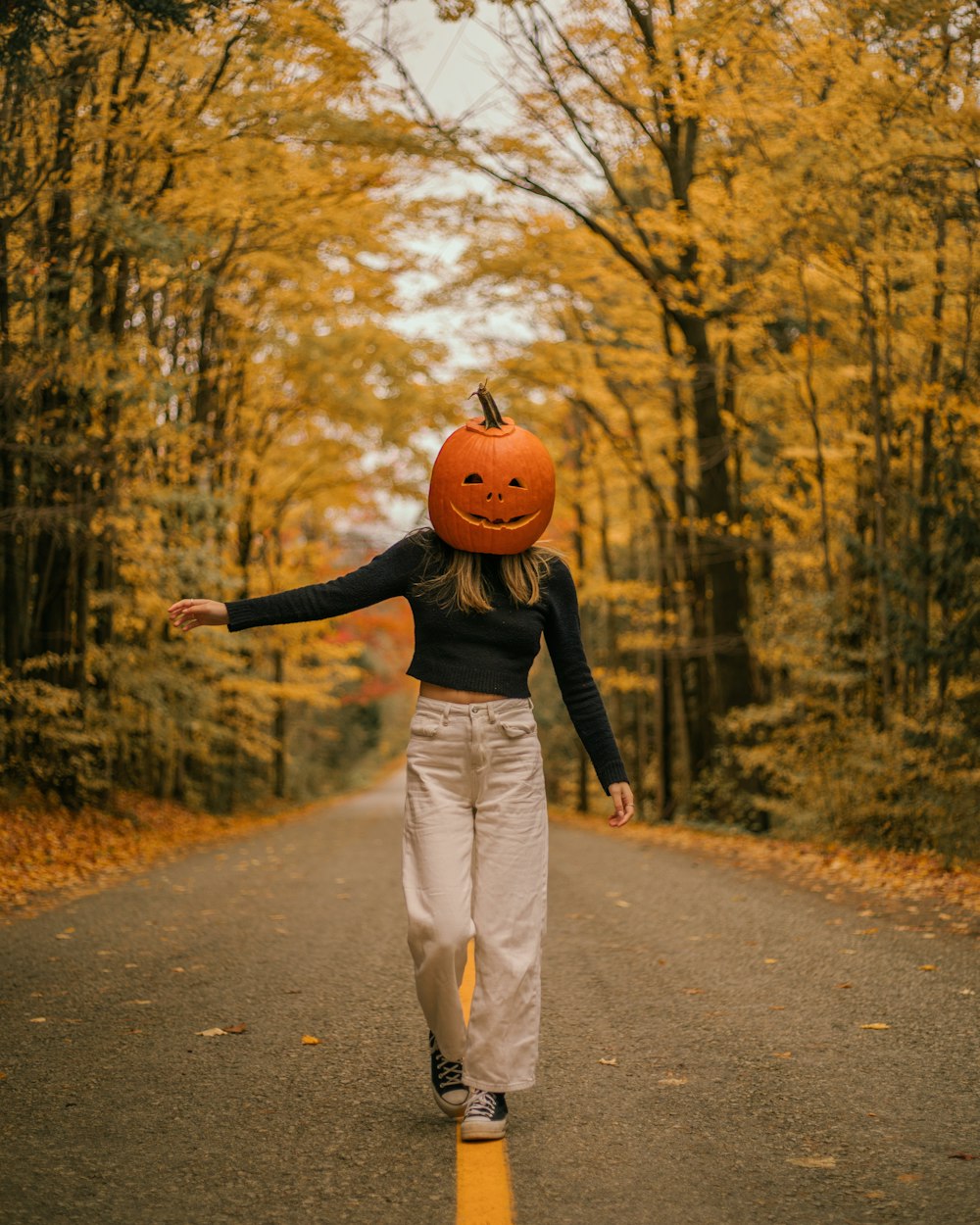 a woman walking down a road with a pumpkin on her head