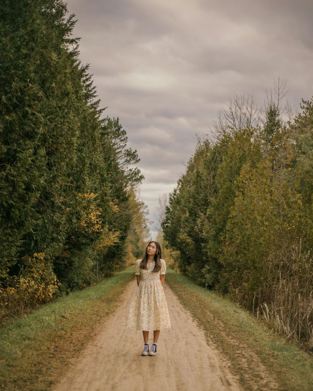 a woman standing on a dirt road surrounded by trees