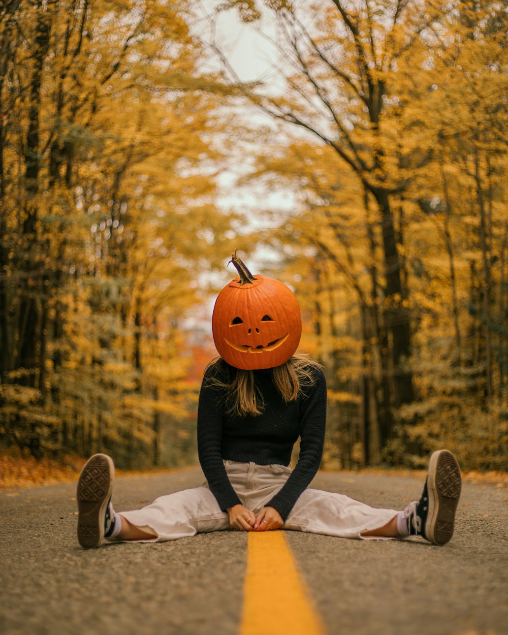a woman sitting on the side of a road with a pumpkin on her head
