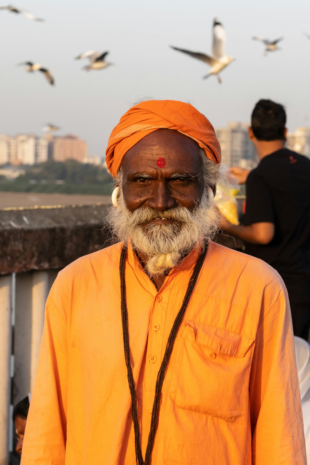 a man wearing an orange turban standing in front of a flock of birds