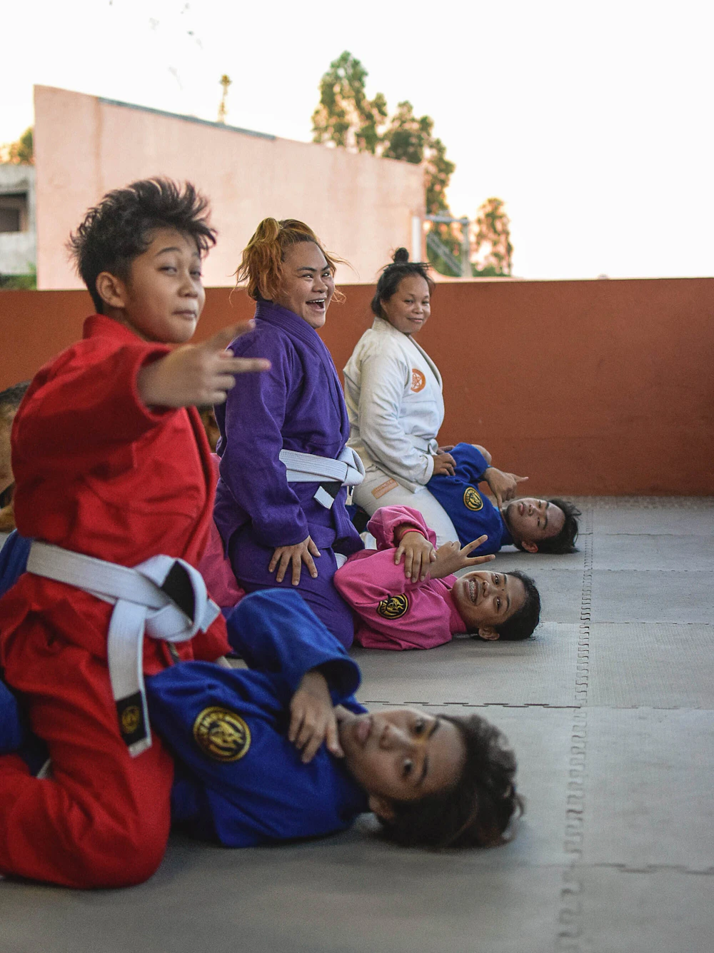 A group of children in colourful gis laughing together on a rooftop mat