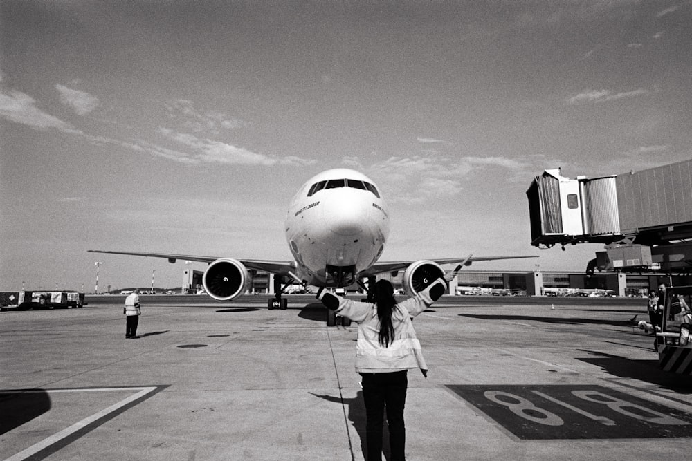 a black and white photo of a woman standing in front of an airplane