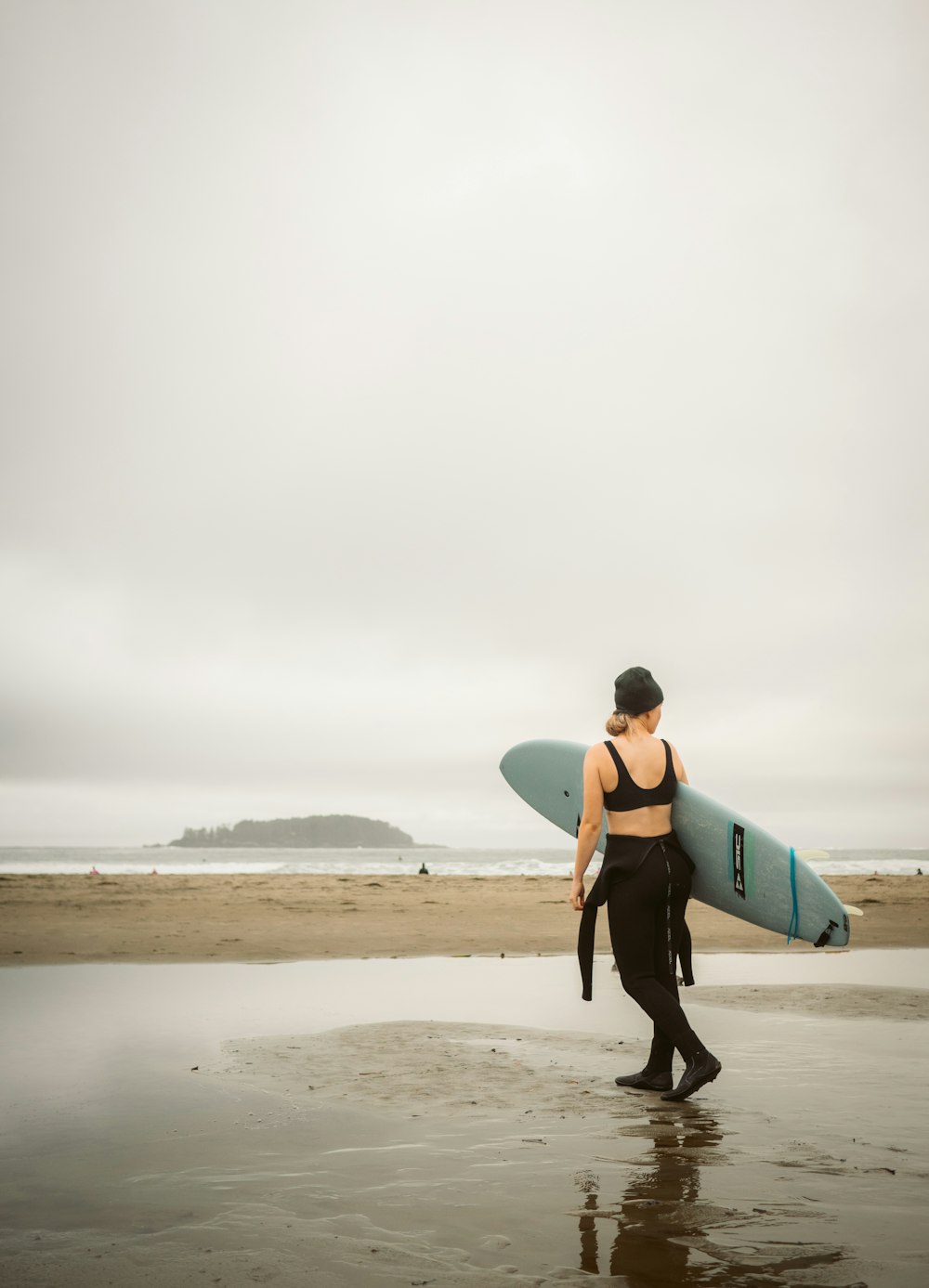 a woman carrying a surfboard on a wet beach