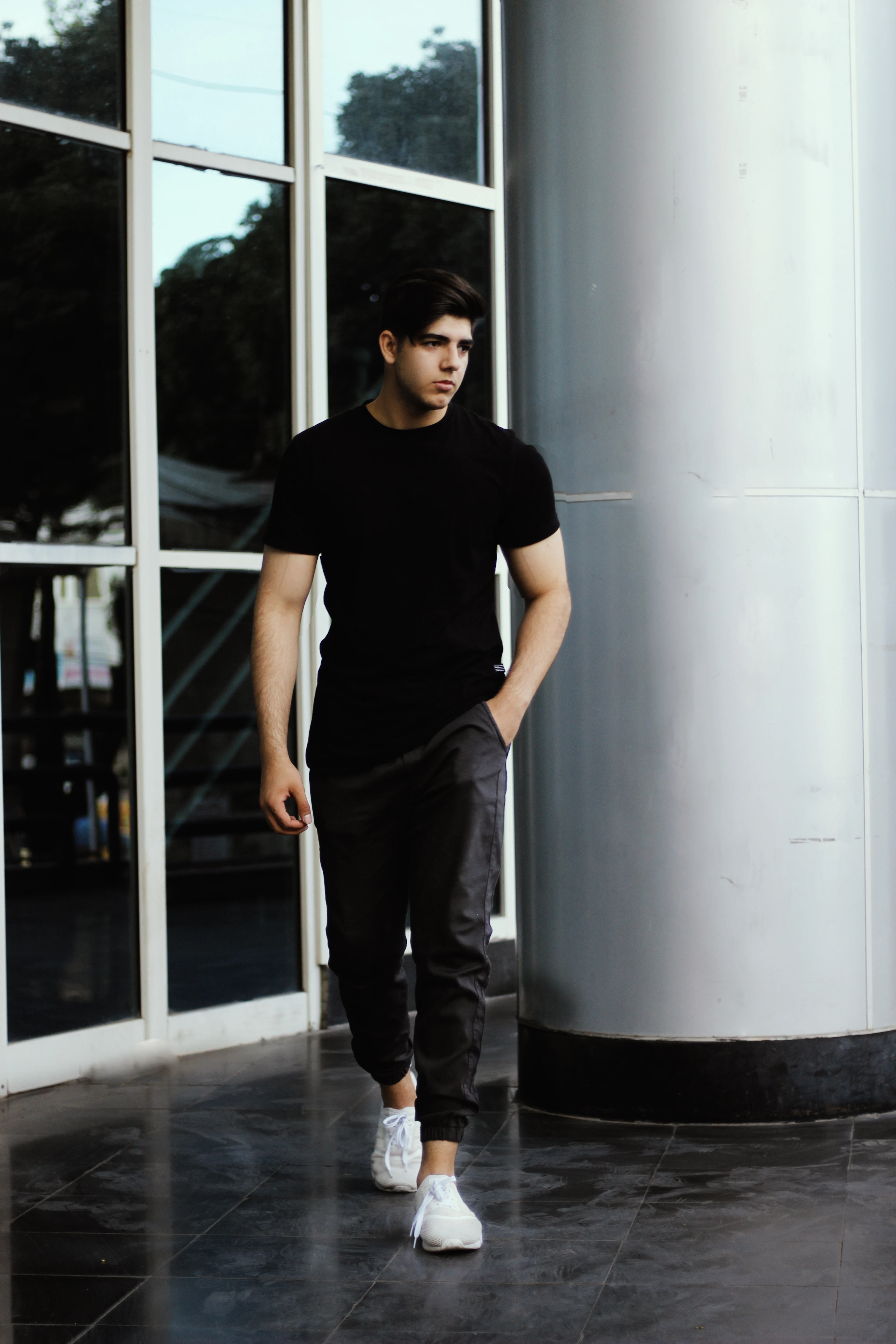 Man in a black tee and black slim joggers walking past glass doors