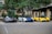 Three high-performance sports cars are parked side by side in an outdoor setting with trees and a building in the background. The cars feature sleek designs and vibrant colors, including black and red, white and blue, and yellow and black.