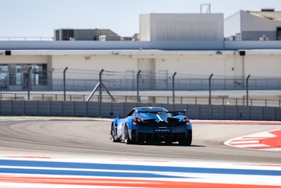 A sleek sports car speeding along the Nürburgring track under a clear blue sky.