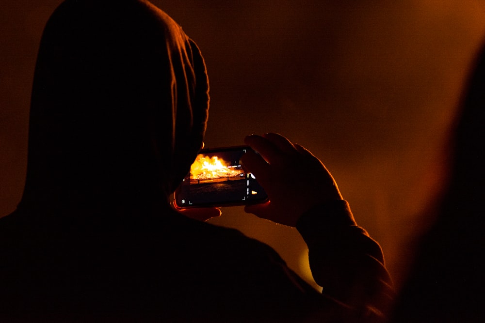 a person in a hoodie taking a picture with a cell phone