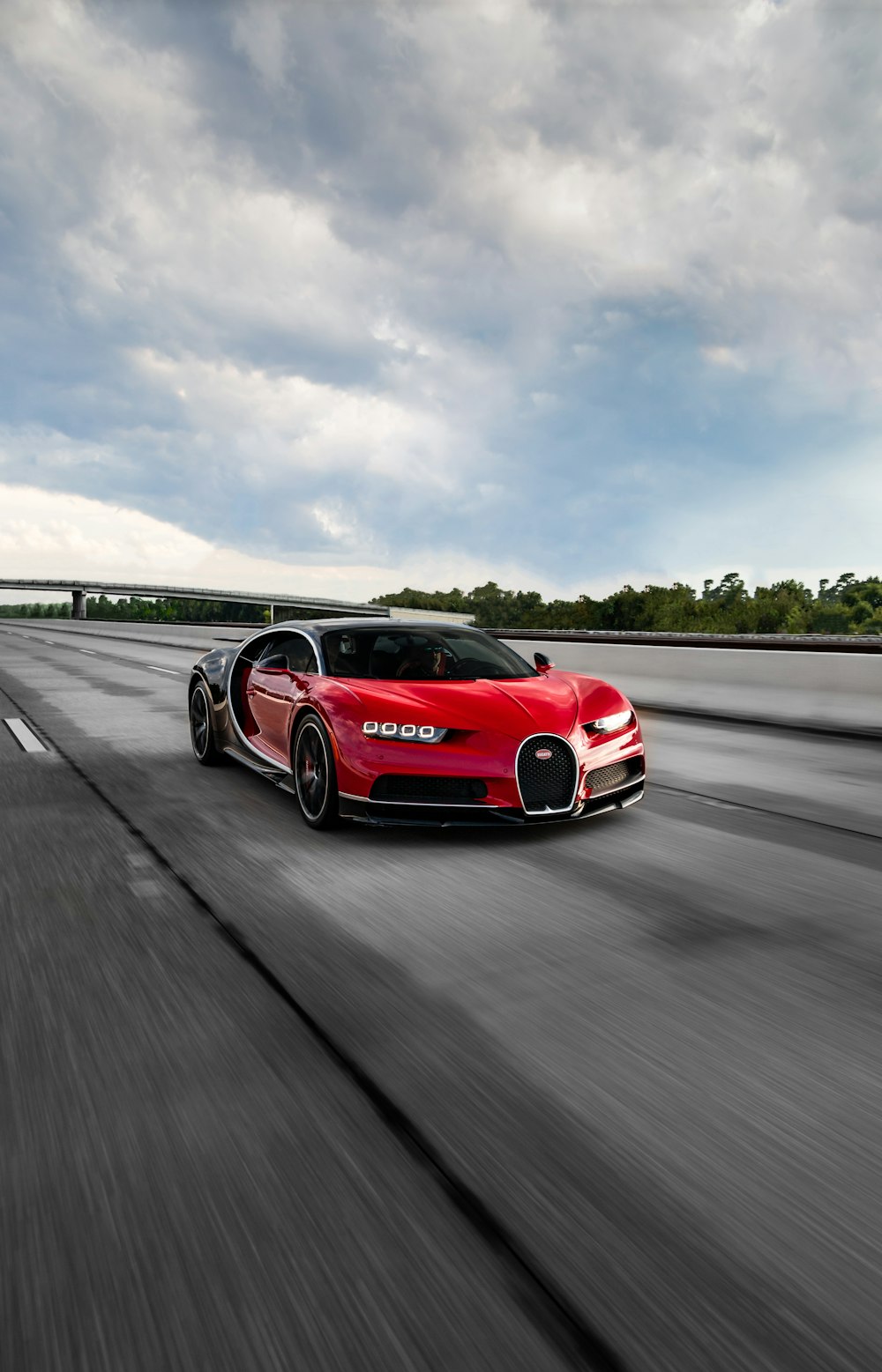 a red bugatti driving down a highway under a cloudy sky