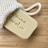 A beige bar of soap with an engraving partially visible emerges from a white mesh bag, placed on a light wooden surface.