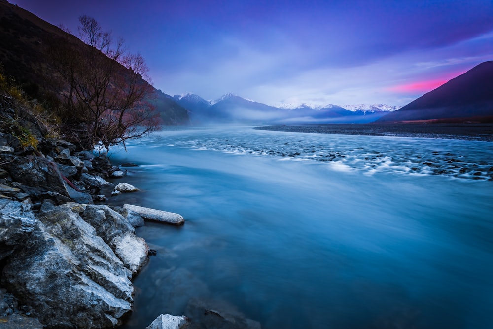 a body of water surrounded by mountains under a cloudy sky