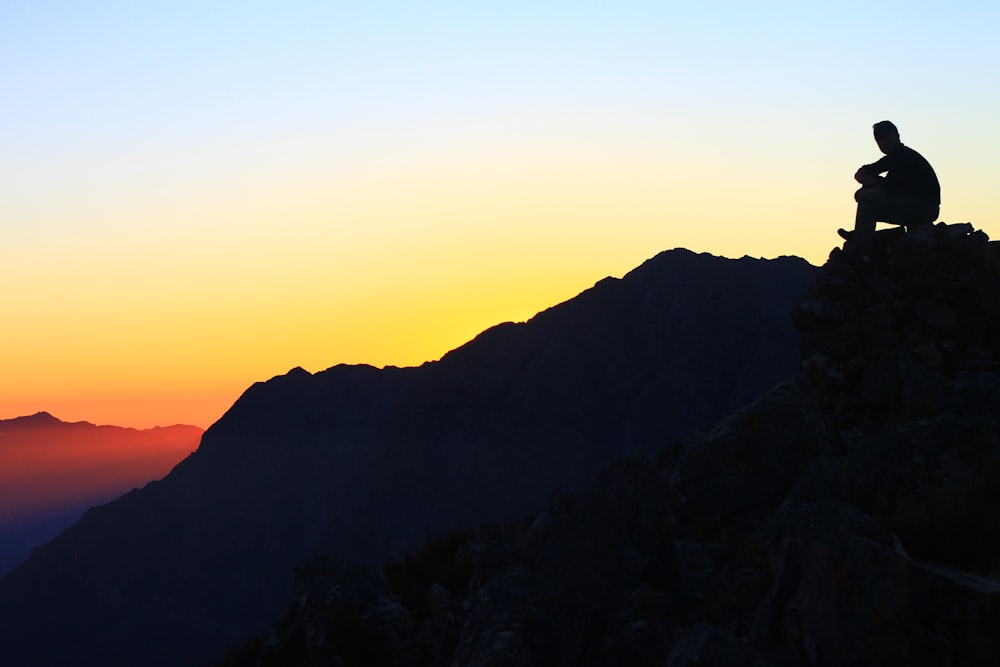 Un uomo seduto sulla cima di una montagna al tramonto