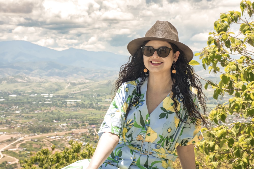 a woman wearing a hat and sunglasses sitting on a rock