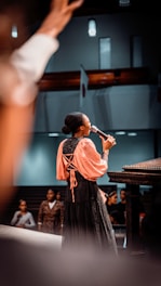 a woman standing in front of a piano while holding a microphone
