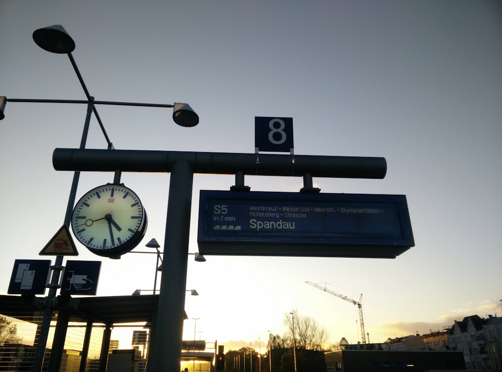 a clock on a pole next to a street sign