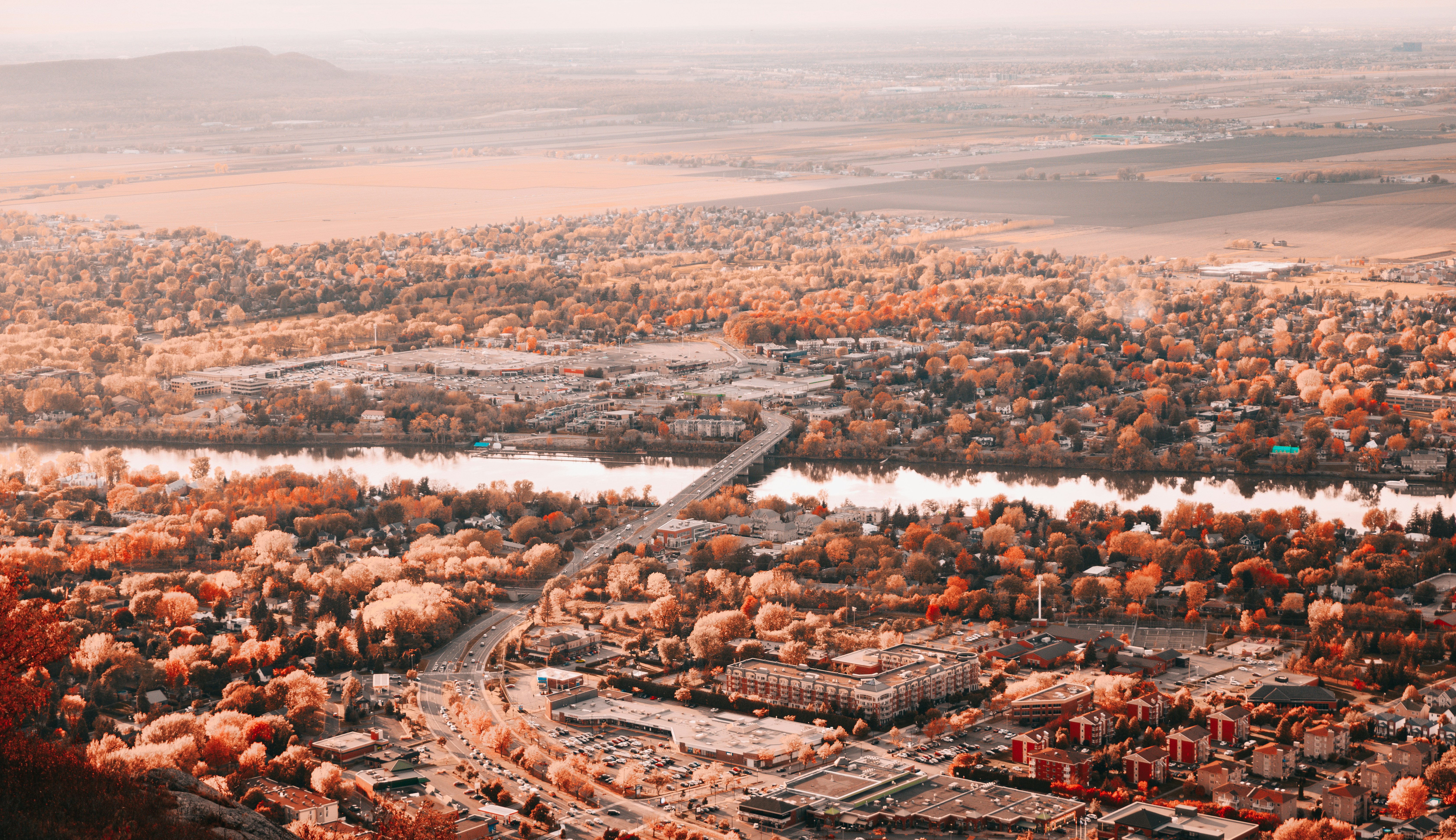 an aerial view of a city surrounded by trees, Landscape of a city with a river during autumn