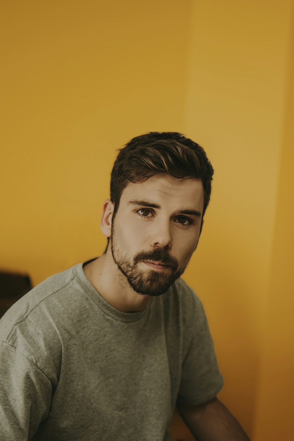 a man with a beard sitting in front of a yellow wall