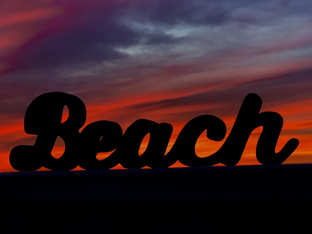 a silhouette of the word beach in front of a sunset