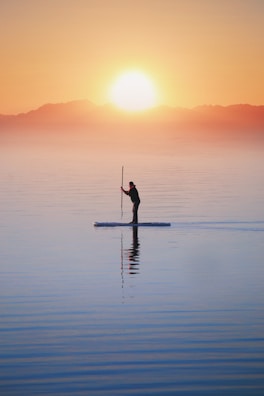 Woman paddling out on a calm ocean at sunrise, wearing sleek manaia swimwear.