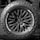 A close-up of a rugged, all-terrain tire mounted on the back of a vehicle featuring bold, deep treads and a multi-spoke wheel design. The brand logo and tire specifications are prominently displayed.
