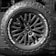 A close-up of a rugged, all-terrain tire mounted on the back of a vehicle featuring bold, deep treads and a multi-spoke wheel design. The brand logo and tire specifications are prominently displayed.