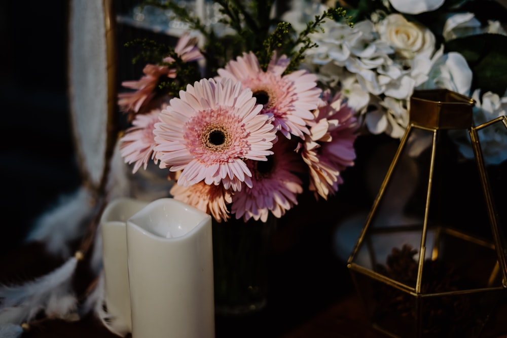 a vase filled with pink and white flowers next to a candle