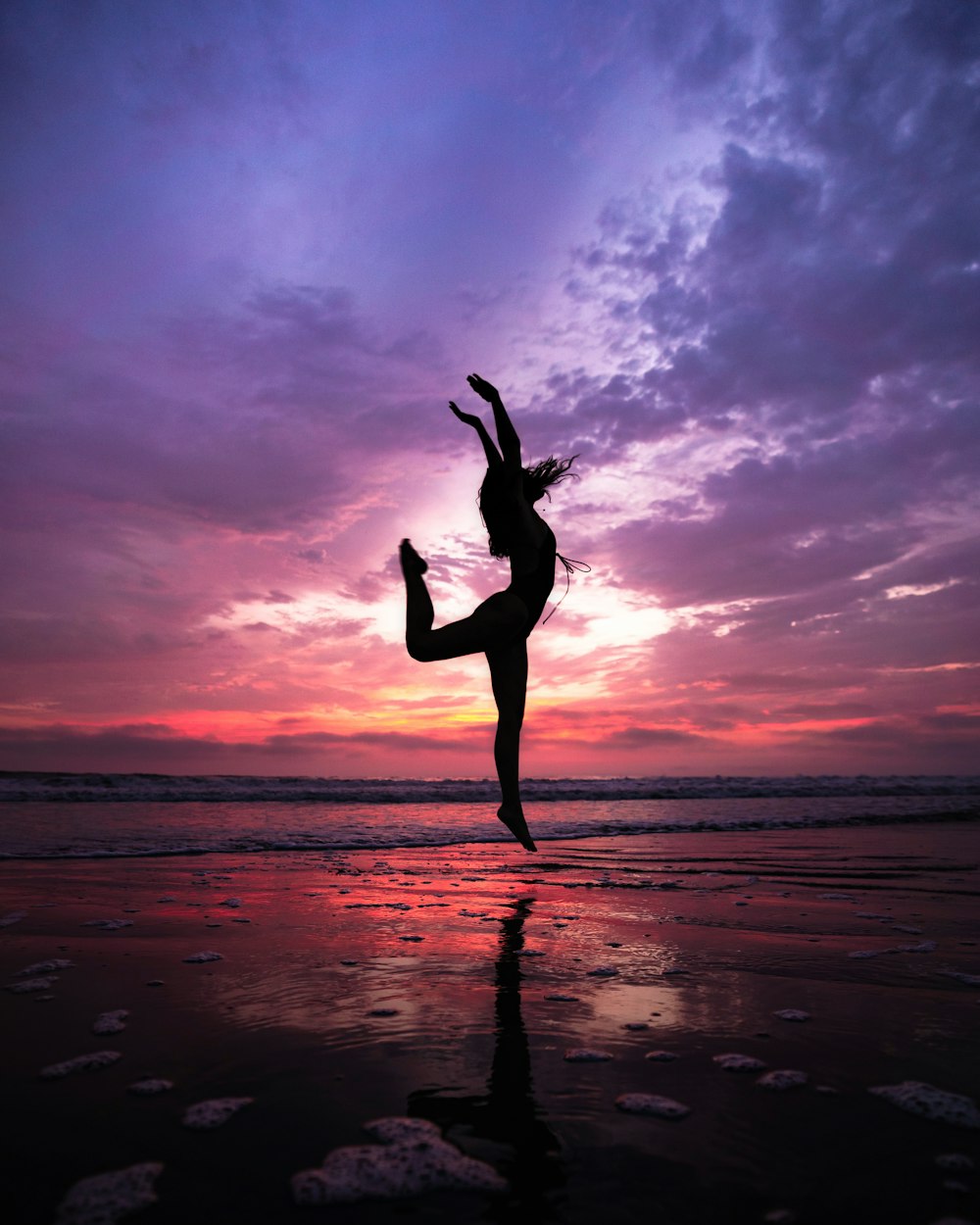 a woman doing a handstand on the beach at sunset