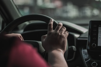 a person driving a car with their hand on the steering wheel