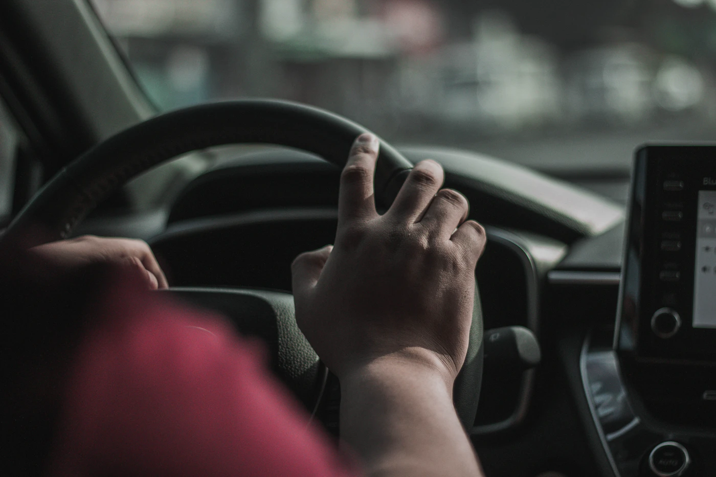 A driver's hands resting on a car steering wheel on an open road.