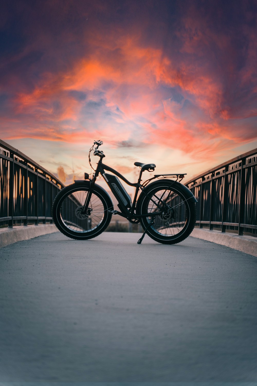 a bicycle parked on a bridge with a sunset in the background