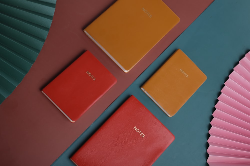three different colored notebooks next to a pink fan