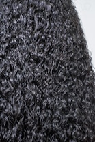 A close-up view of dark, tightly coiled curly hair with a glossy texture. The curls are prominent, well-defined, and densely packed, creating a detailed and uniform pattern.