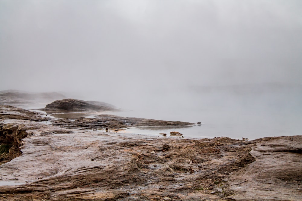 a body of water surrounded by rocks and fog