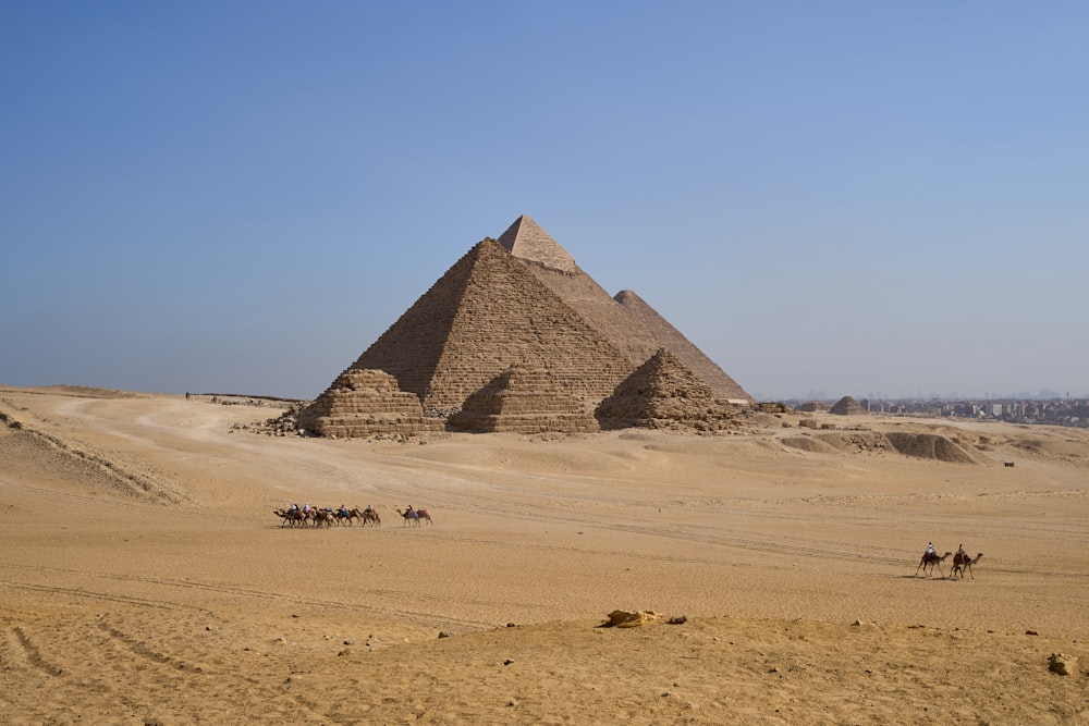 a group of people riding camels in front of a pyramid