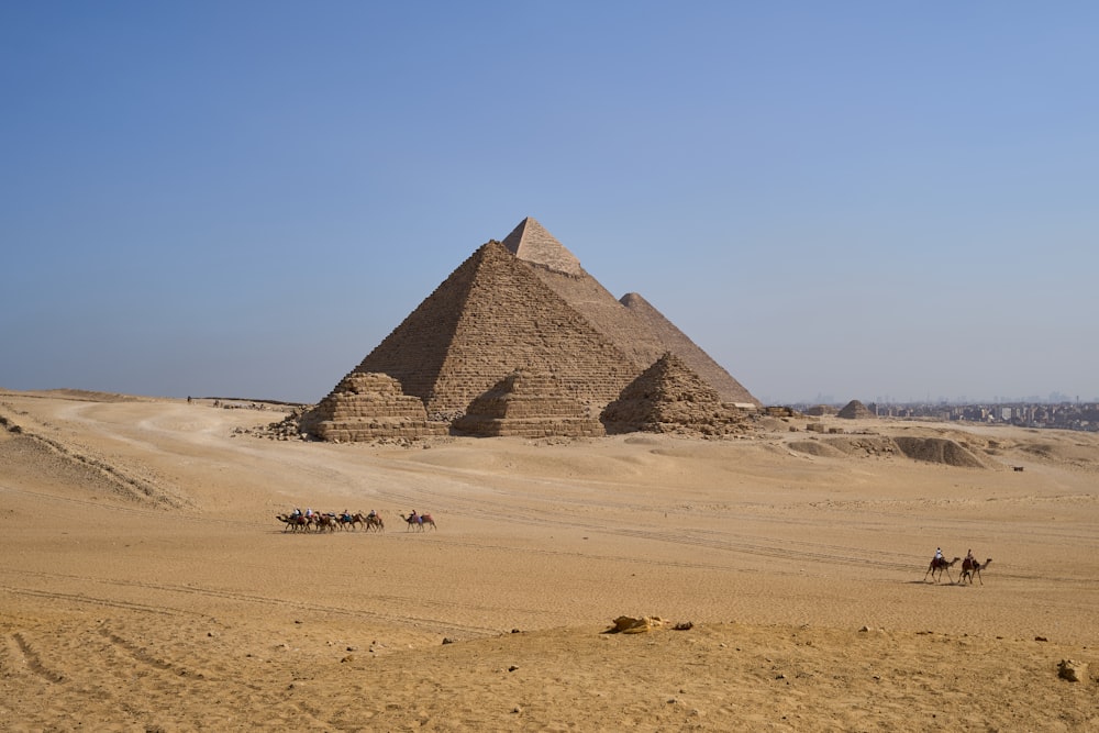 um grupo de pessoas montando camelos na frente de uma pirâmide